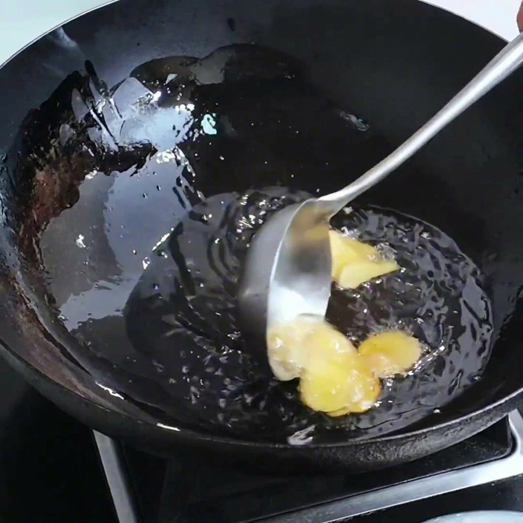 Ginger slices and shrimp heads sizzling in a wok with hot oil.