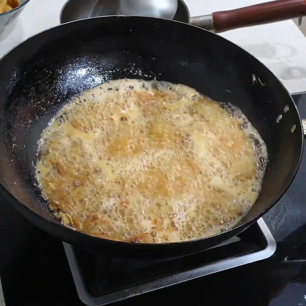 Salt being sprinkled into a bubbling, golden-orange shrimp broth.