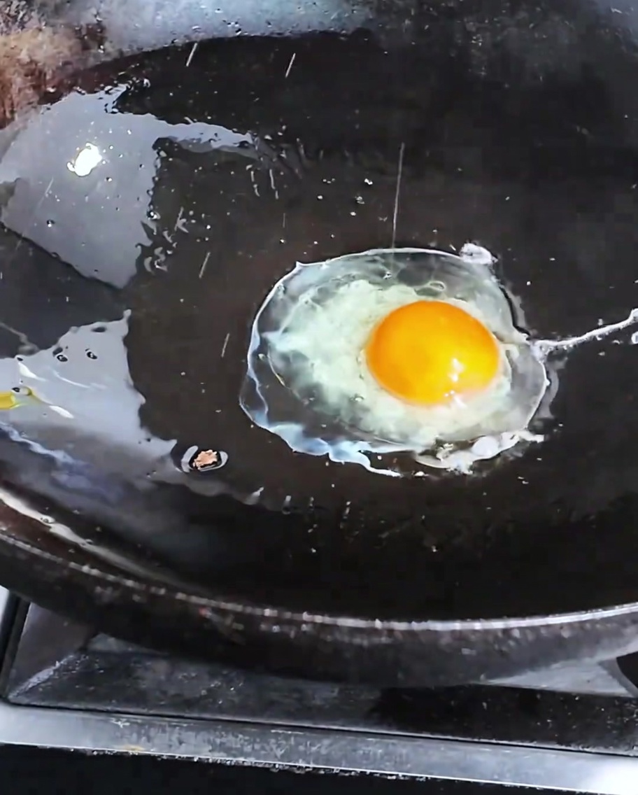 A single egg frying in a hot, dark wok.