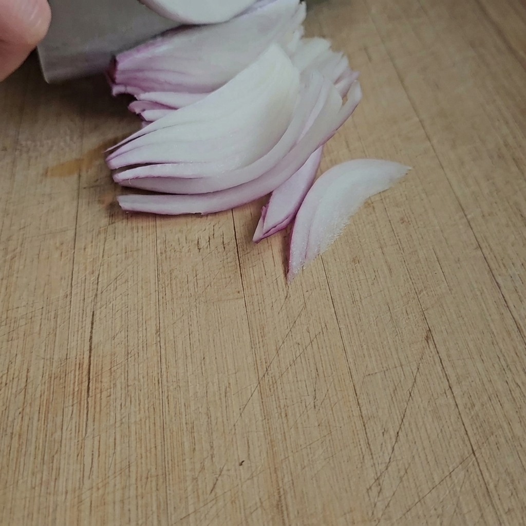 Thin slices of fresh ginger prepared on a wooden cutting board.