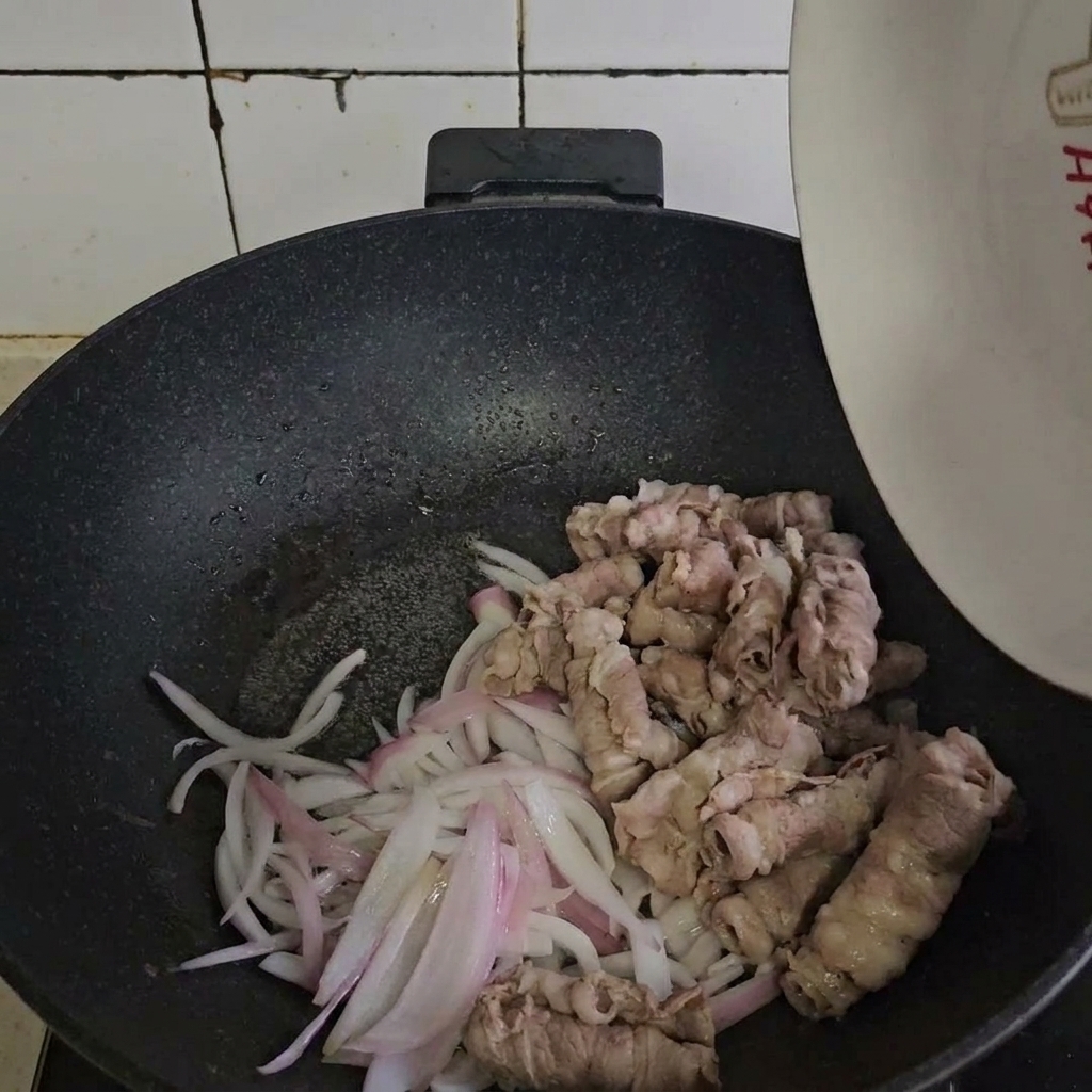 Blanched beef rolls being combined with sautéed onions in a hot pan.