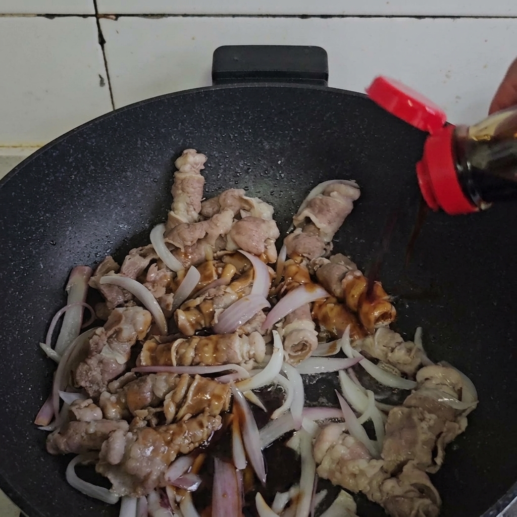Beef and onions being tossed with sauce in a hot pan.