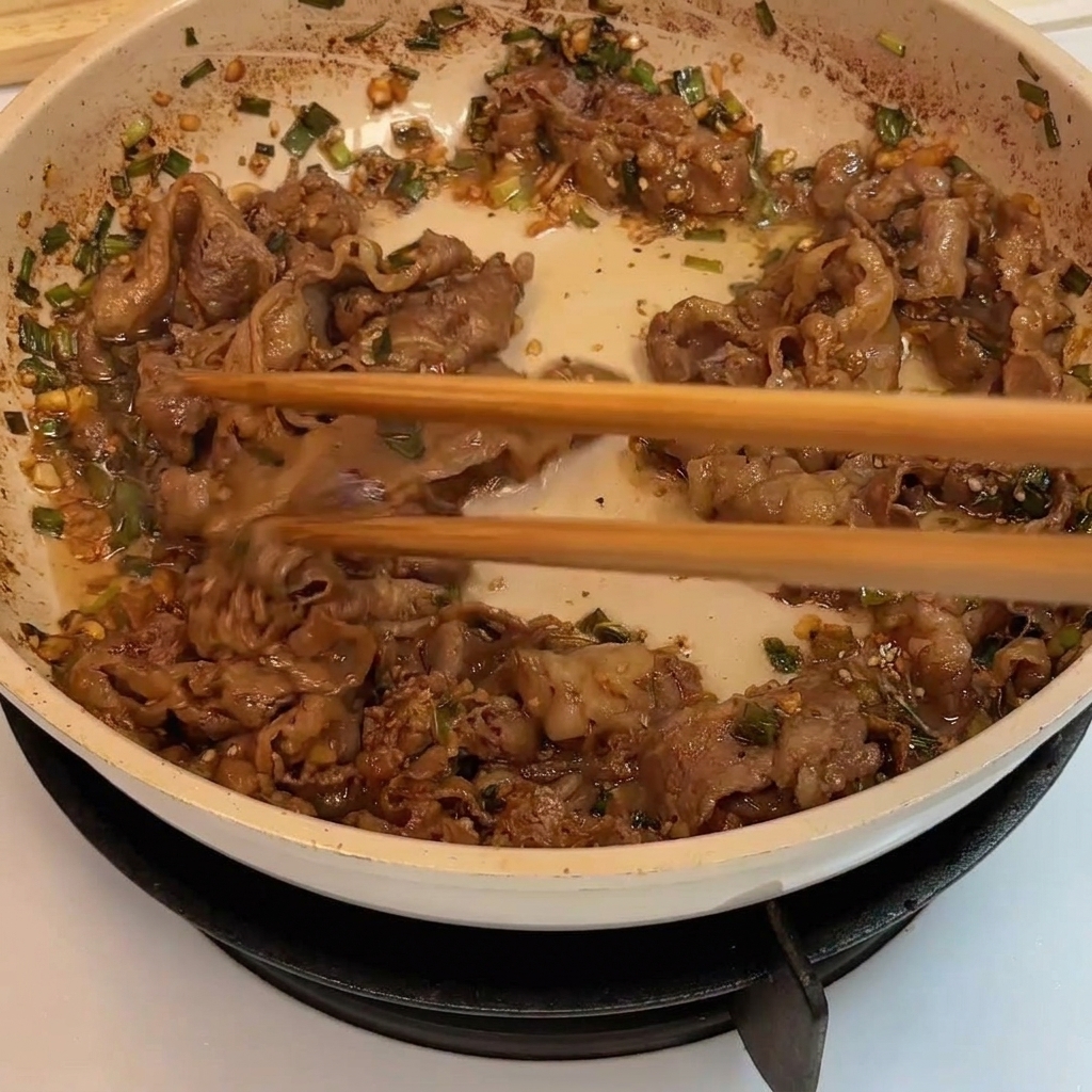 Slices of beef being stir-fried in a pan until browned and cooked through.