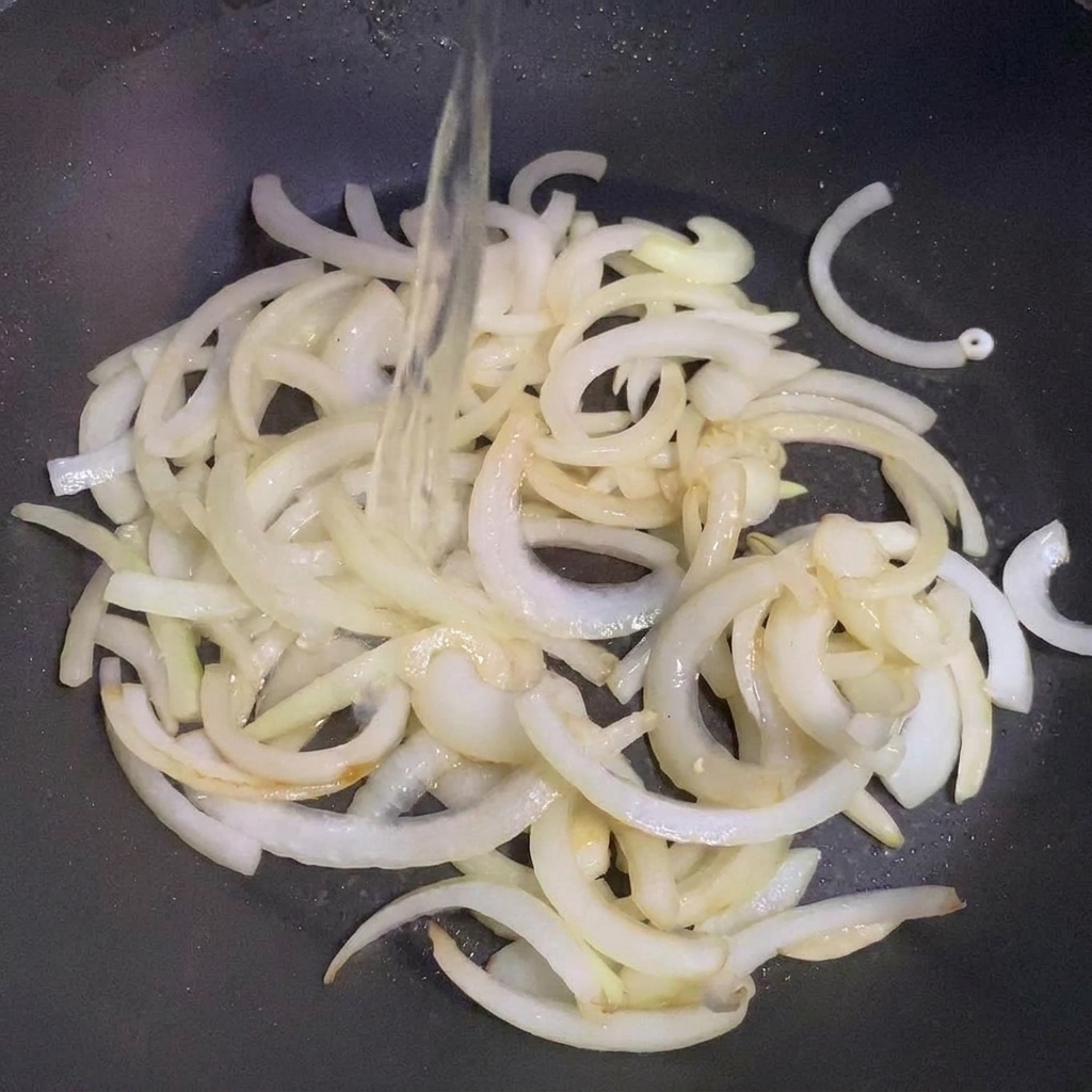 Sake being poured over sautéed onions in a pan.