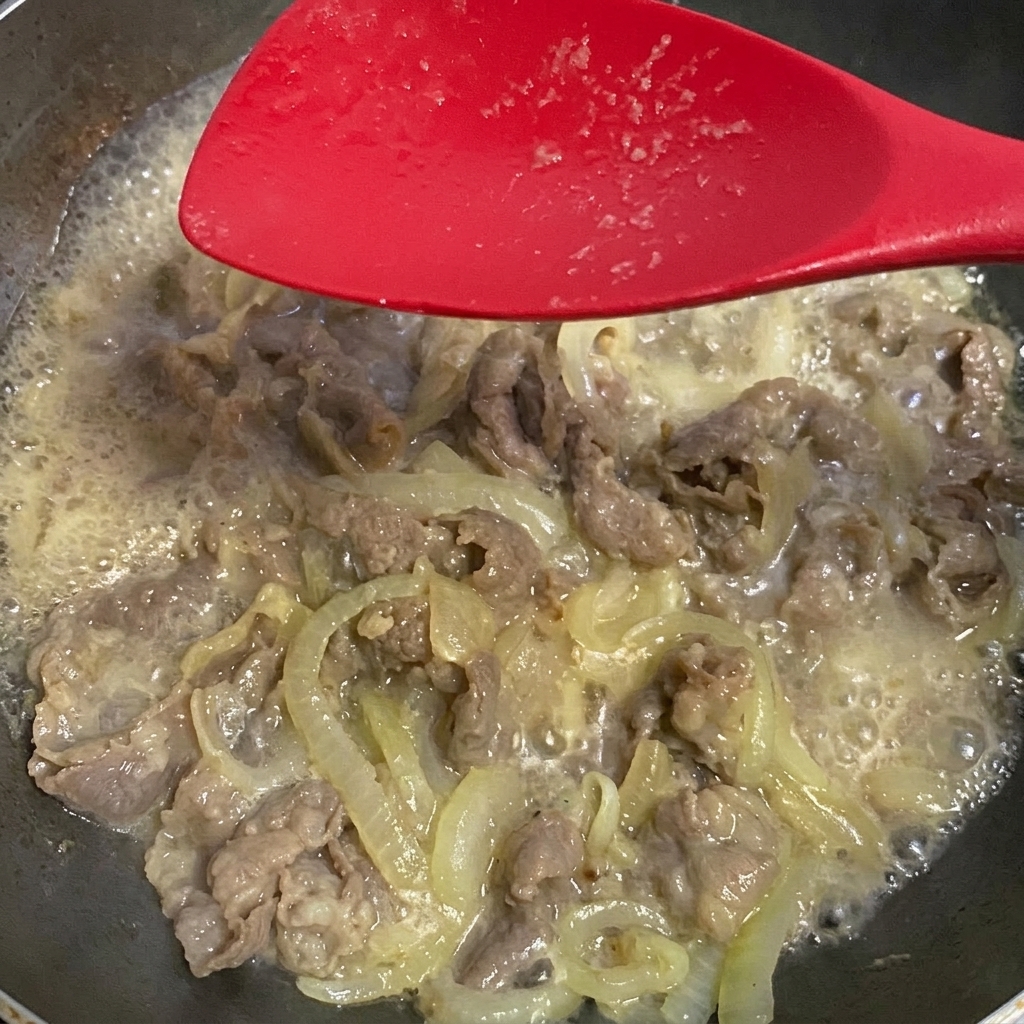 Soy sauce being added to the simmering beef and onion mixture.