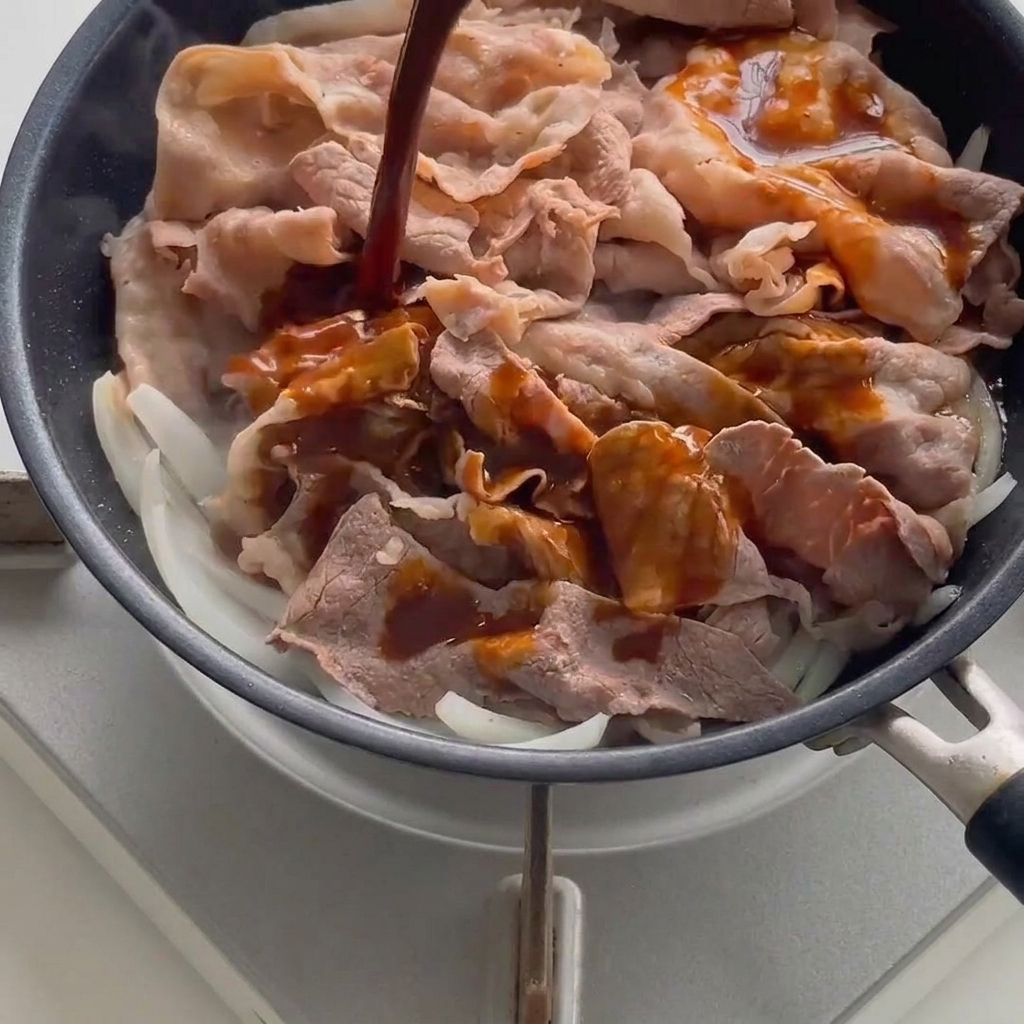 Dark savory sauce being poured over blanched beef and onions in a hot pan.