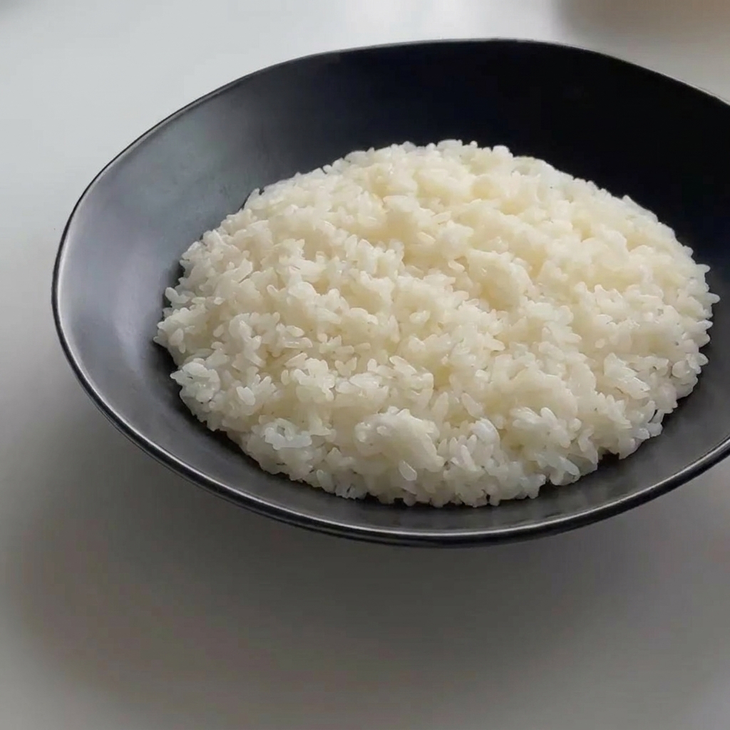 A perfectly cooked egg resting on a mound of white rice in a black bowl.