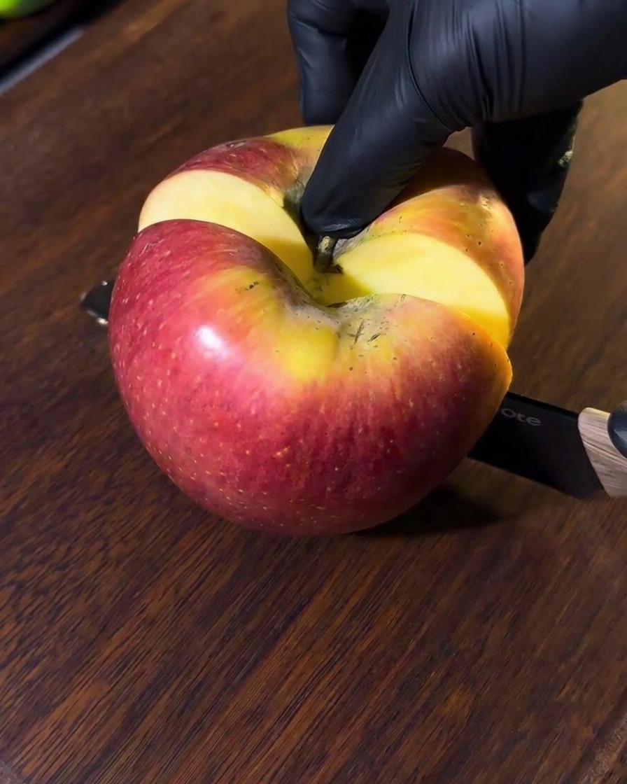 An apple being sliced on a wooden cutting board, with visible pieces ready for the blender.