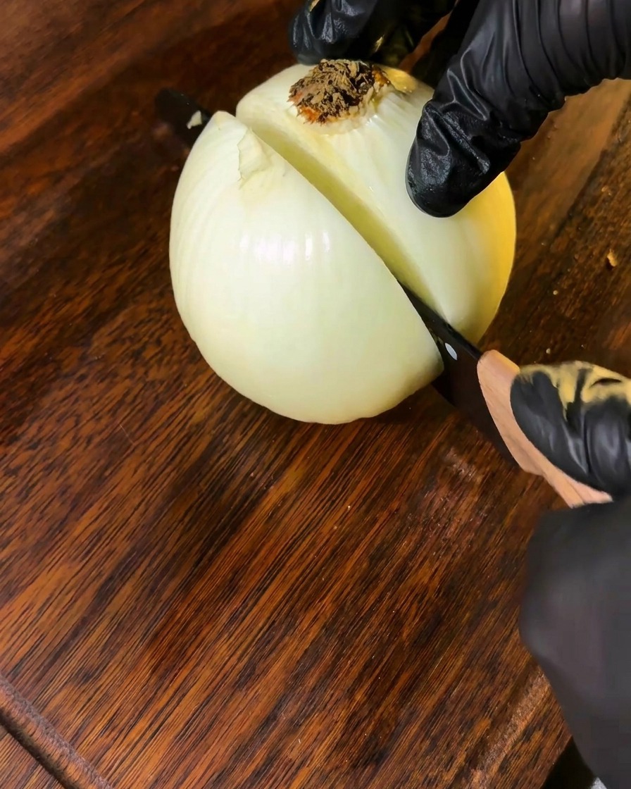 An onion being sliced on a wooden cutting board, with cut sections ready to be used.