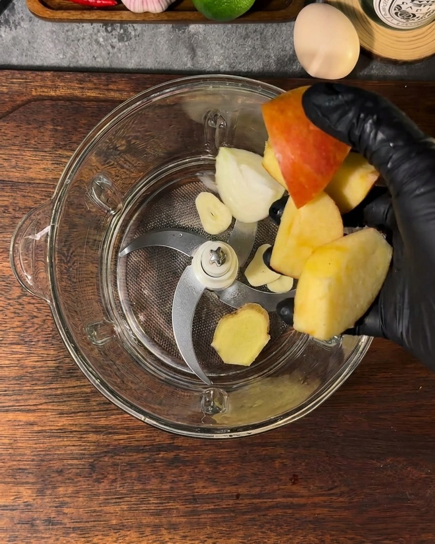 A blender container filled with apple pieces, onion segments, garlic, ginger, and water.