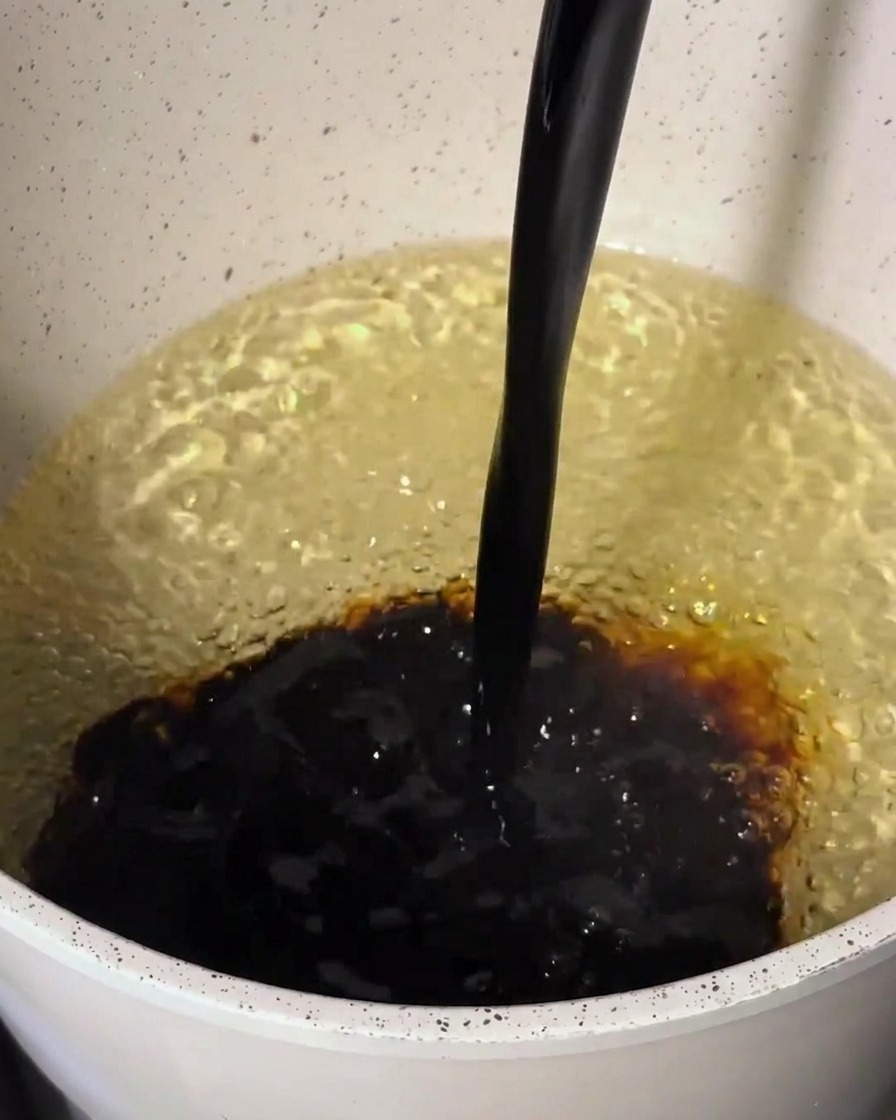 Dark sauce ingredients being poured into a pot containing a lighter base, creating a swirling mixture.