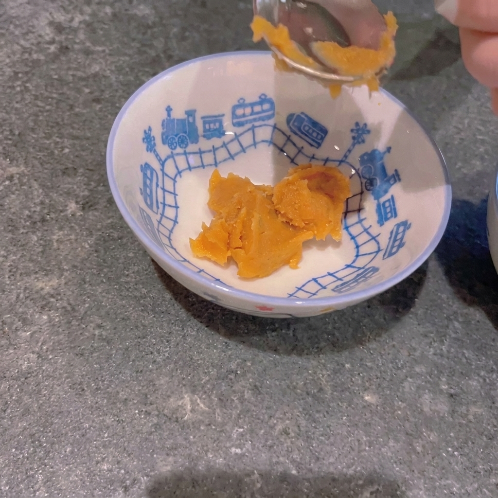 A spoonful of yellow miso paste being placed into a small, train-patterned bowl.
