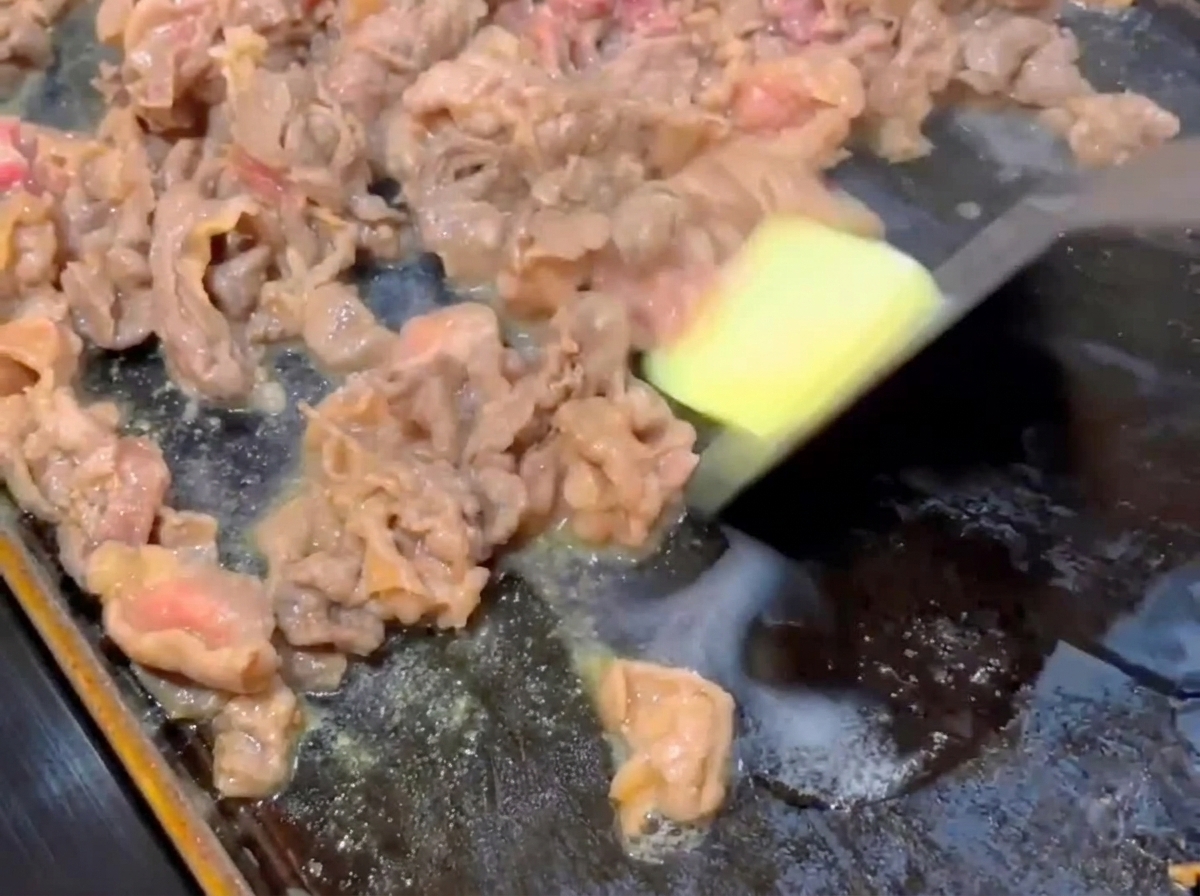 A small square of butter melting onto partially cooked beef slices on a hot flat pan.