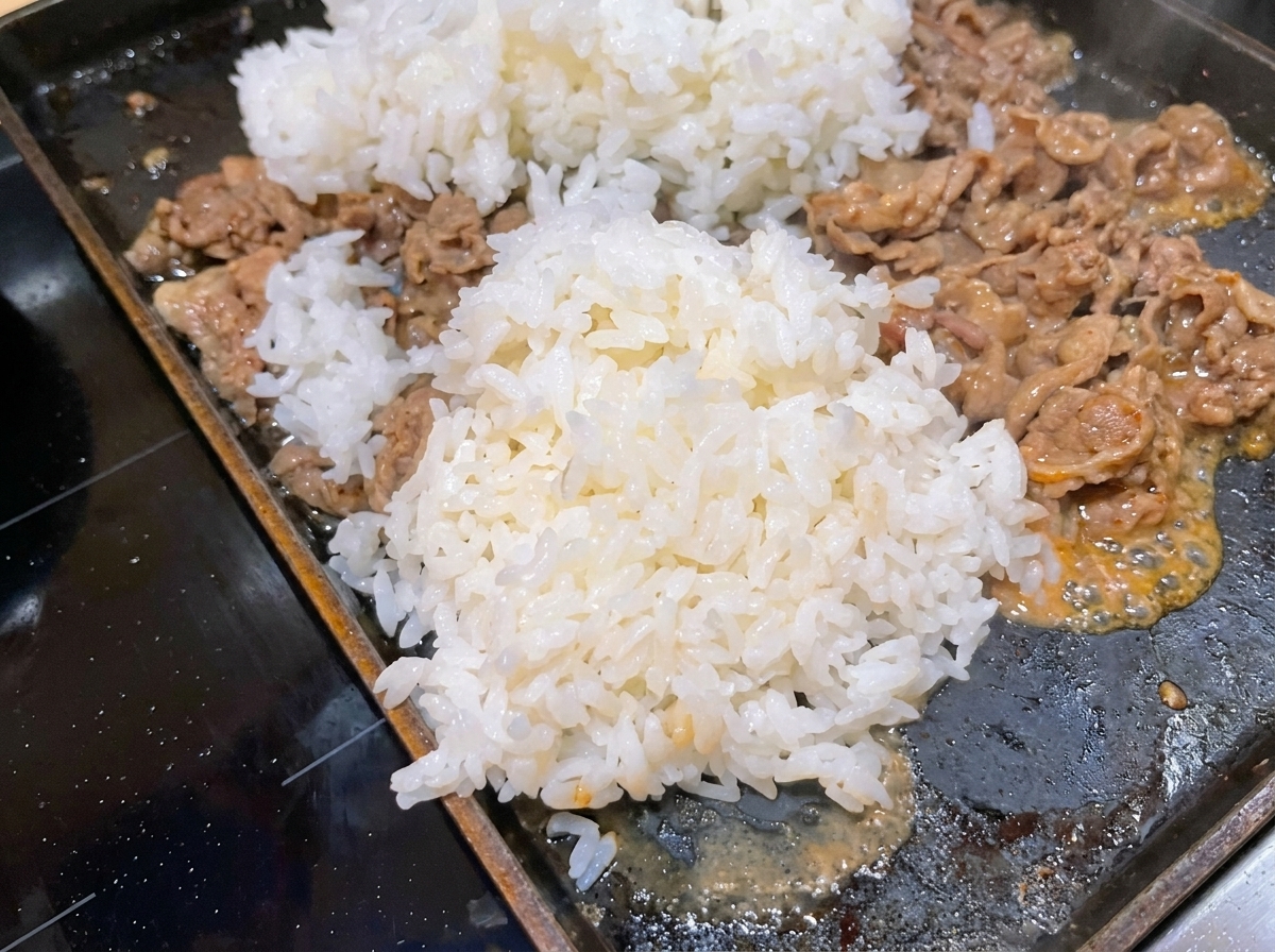 A large mound of cooked white rice added to a hot pan with cooking beef.