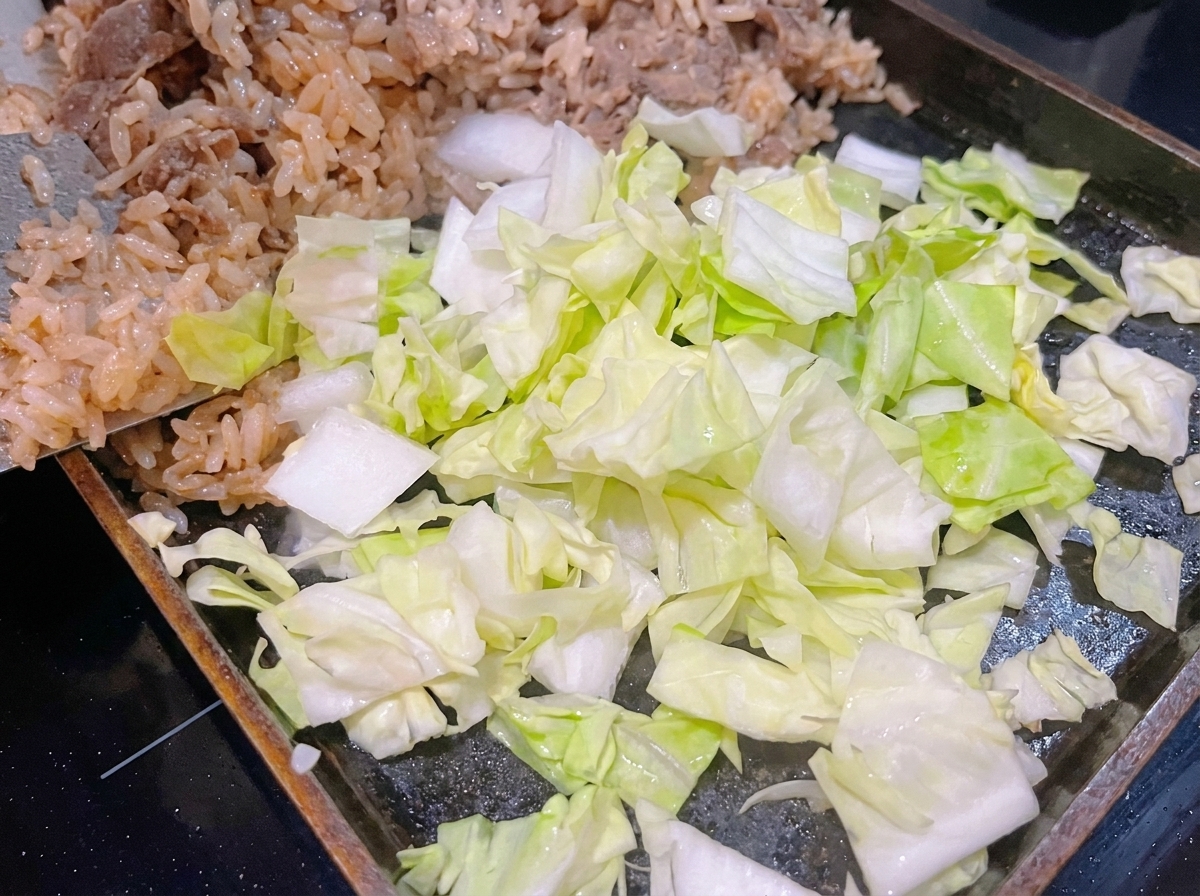Freshly chopped green cabbage placed on top of white rice and beef on a hot cooking pan.