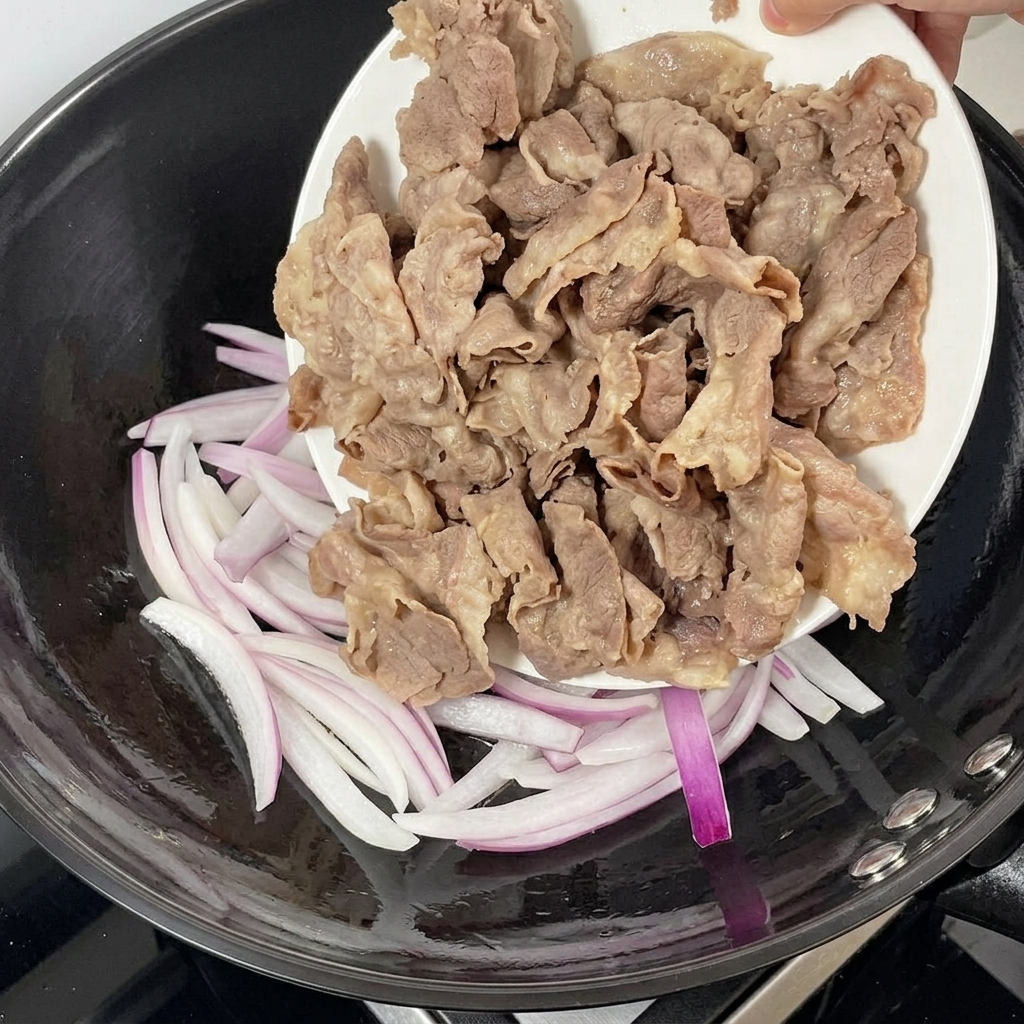 Blanched beef being added to a pan with stir-fried red onions.