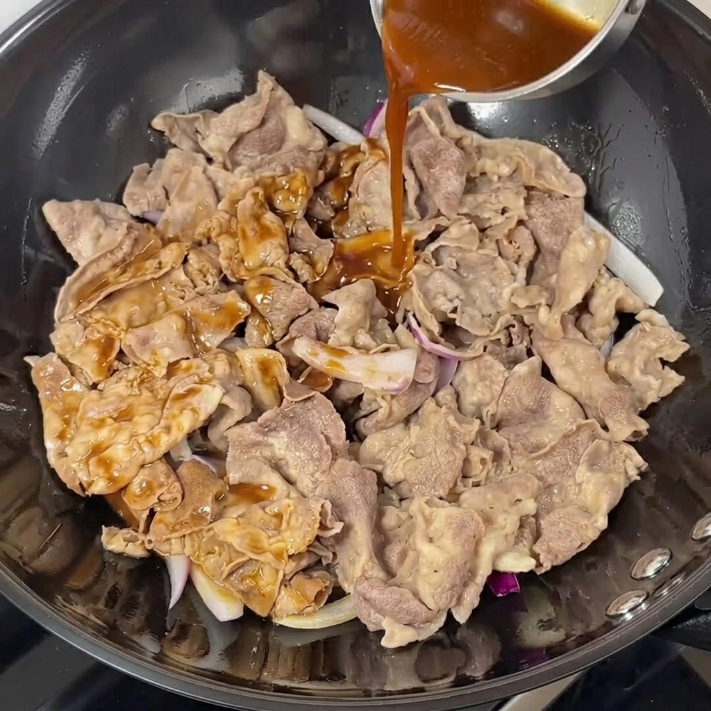 Dark teriyaki sauce being poured over beef and onions in a wok.