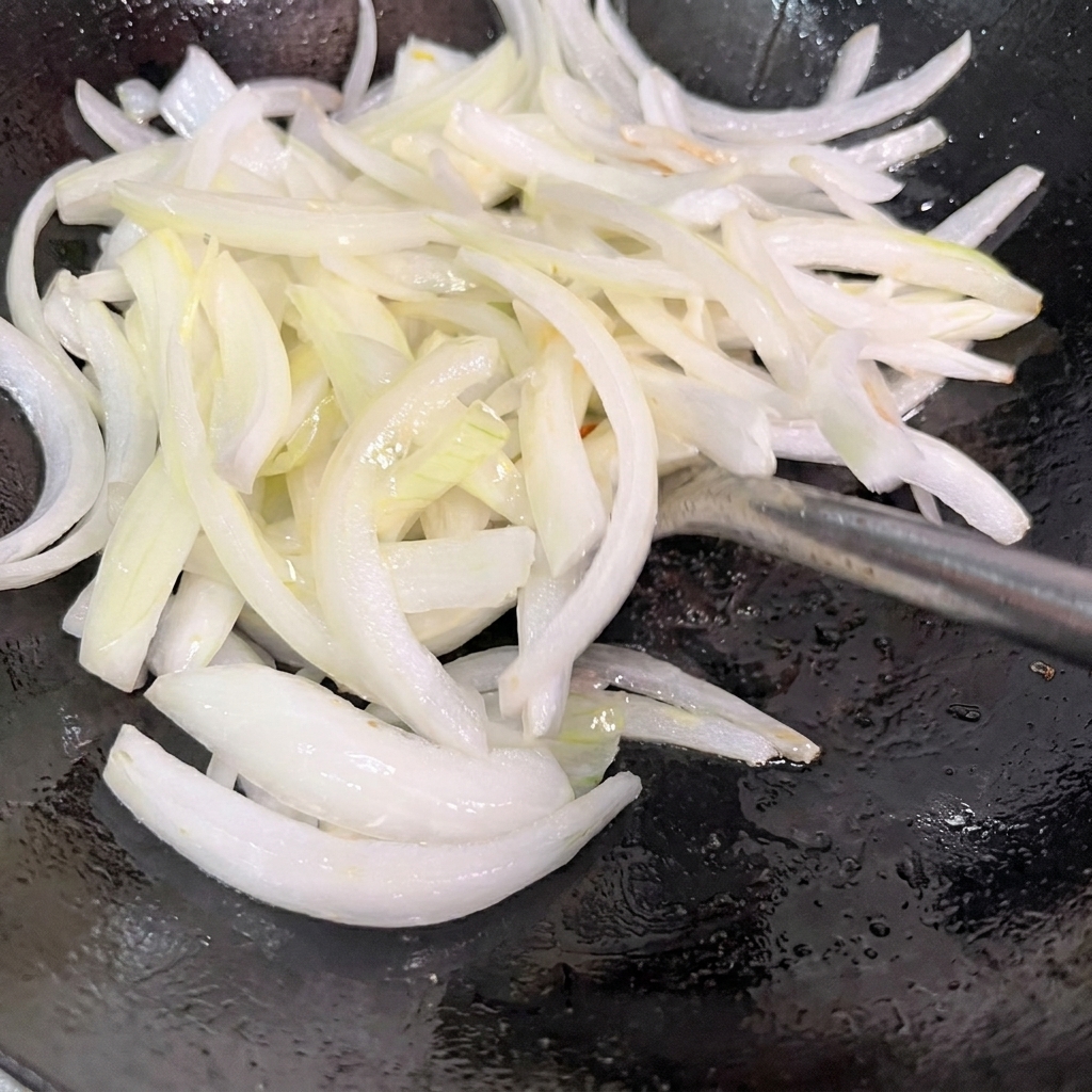 Sliced onions being stir-fried in a hot wok.