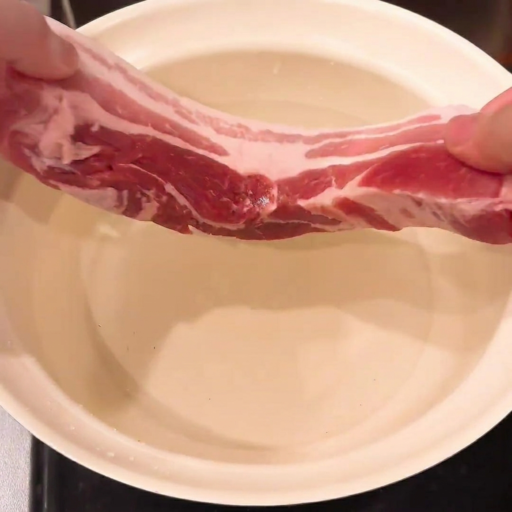 Pork belly, green onion, and ginger submerged in a pot of water, ready for blanching.