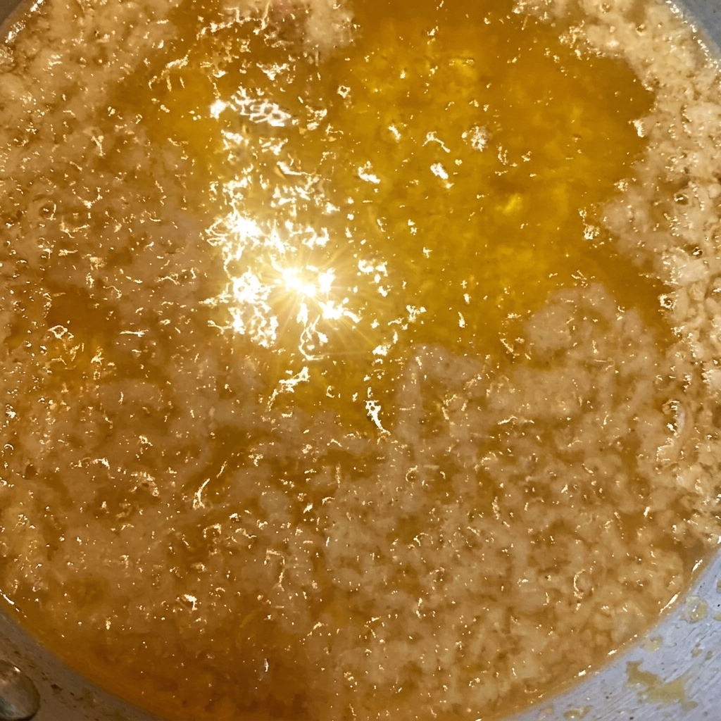 A close-up of crispy, golden-brown tempura flakes being scattered over a bowl of rice already glistening with a dark soy-based sauce.