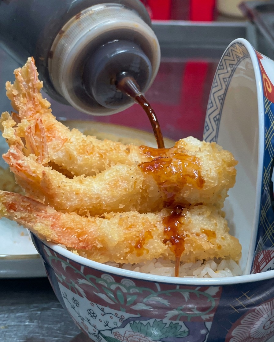 Dark sauce being drizzled from a squeeze bottle onto fried shrimp.