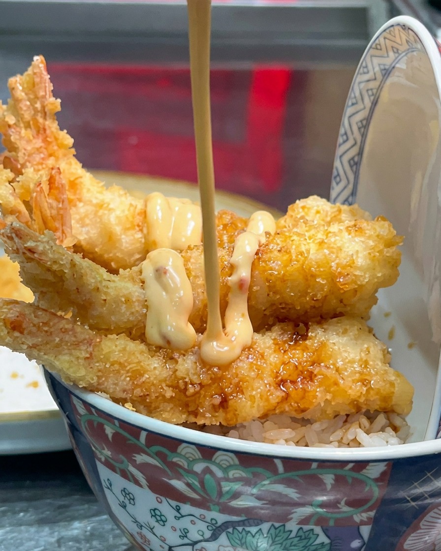 Creamy light-orange sauce being drizzled over the fried shrimp.