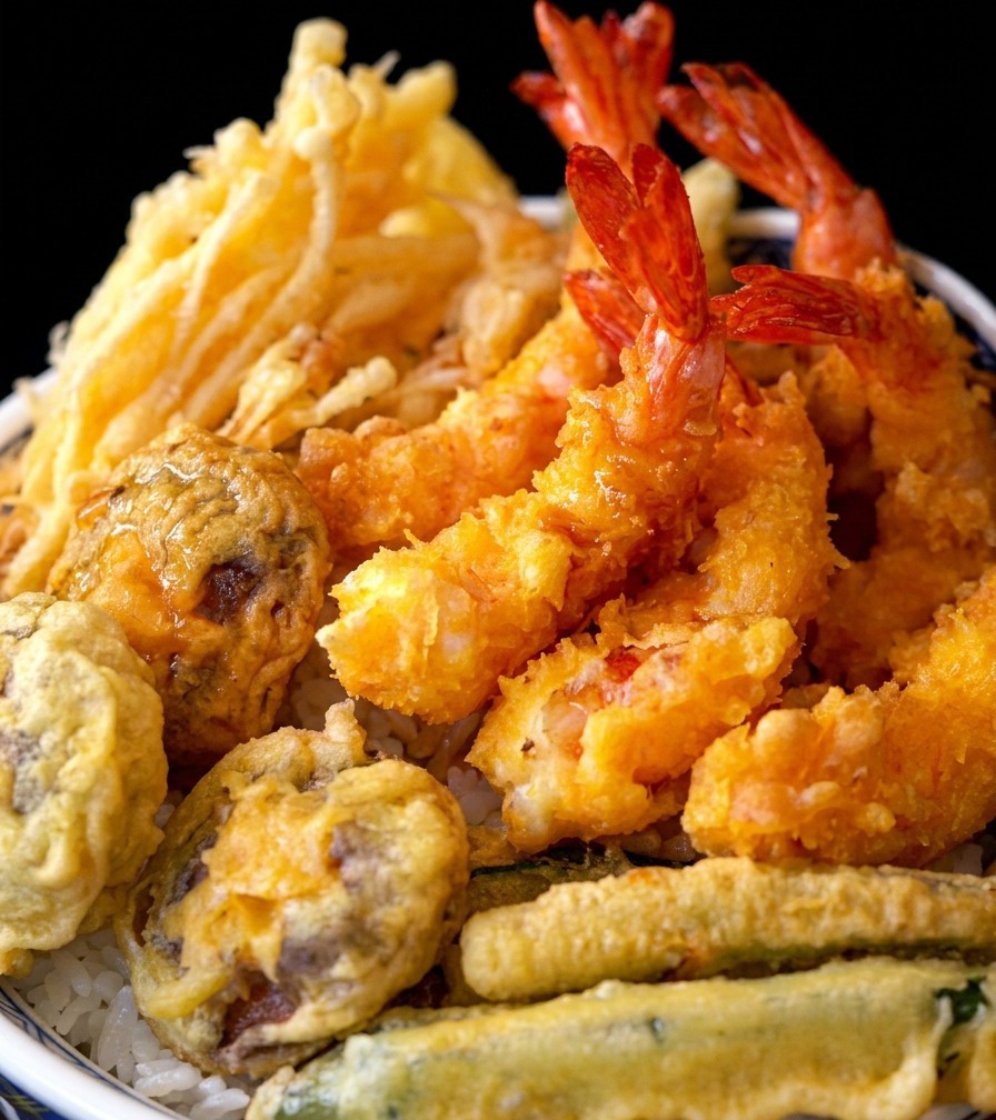 A finished tempura rice bowl topped with crispy fried shrimp and vegetables.