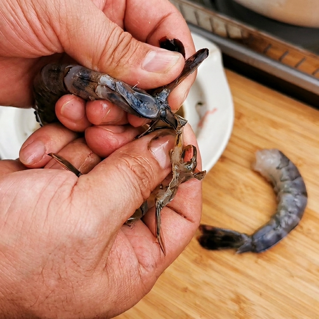 Close-up of hands peeling a raw shrimp while keeping the tail attached.