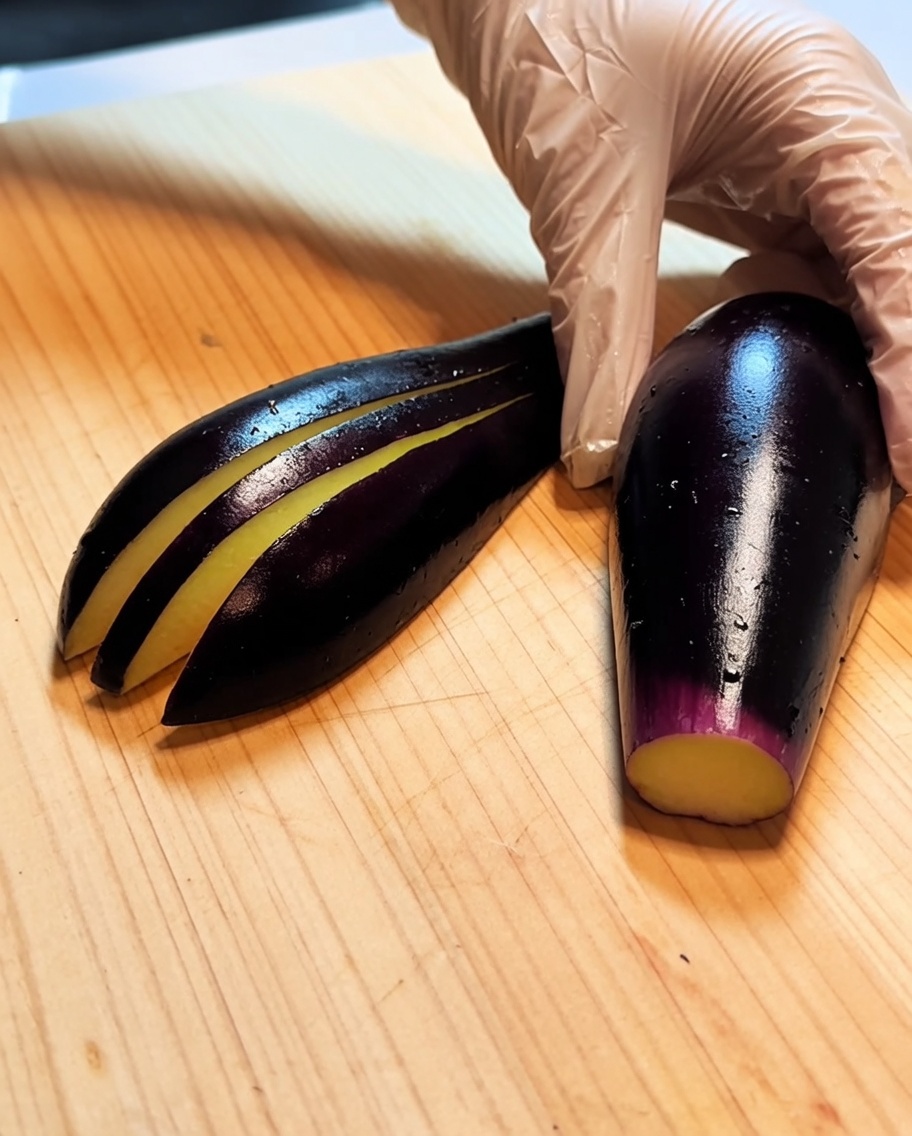 An eggplant on a wooden board with several parallel, shallow cuts along its length.