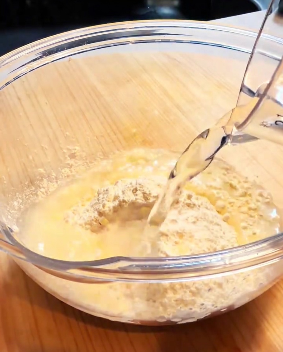 A glass bowl containing tempura flour and water, being whisked to form a smooth, light batter.