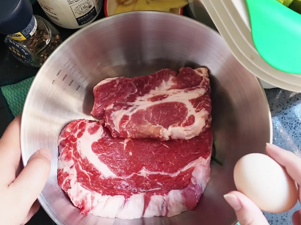 A raw egg being cracked over fresh pork chops in a stainless steel mixing bowl.