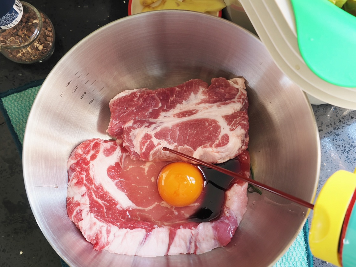 Dark soy sauce and seasonings being poured over pork chops and egg in a bowl.