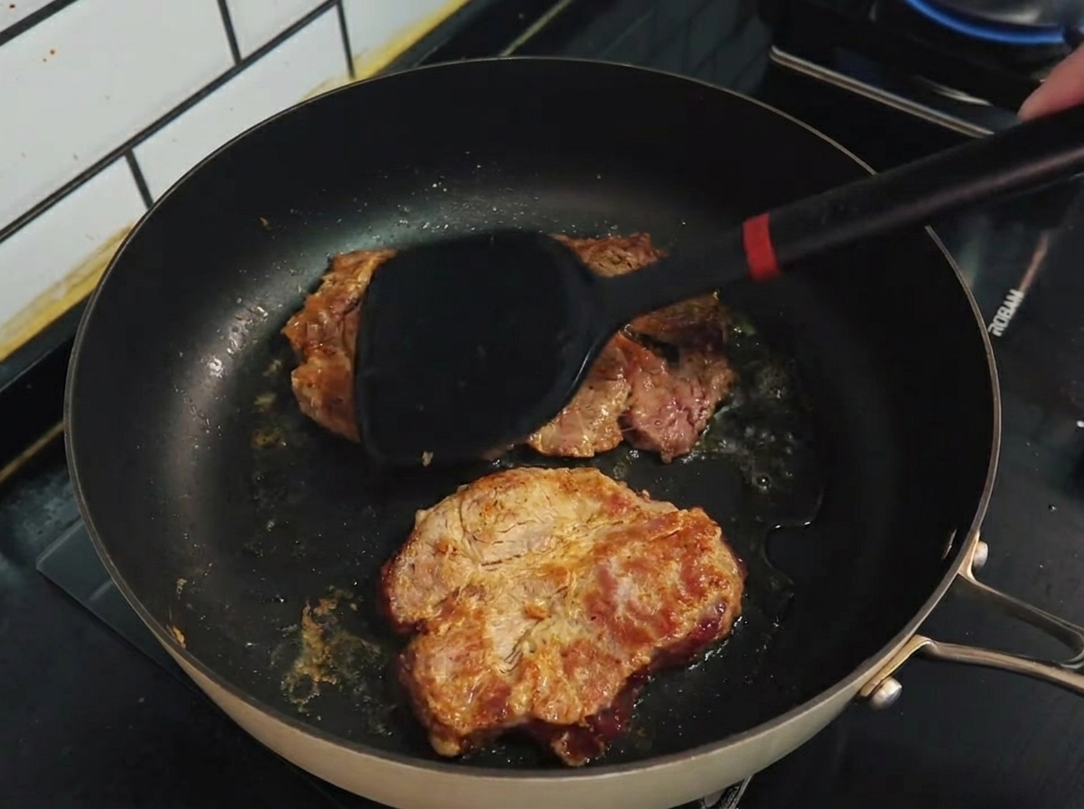 Spatula flipping browned pork chops in a non-stick frying pan.