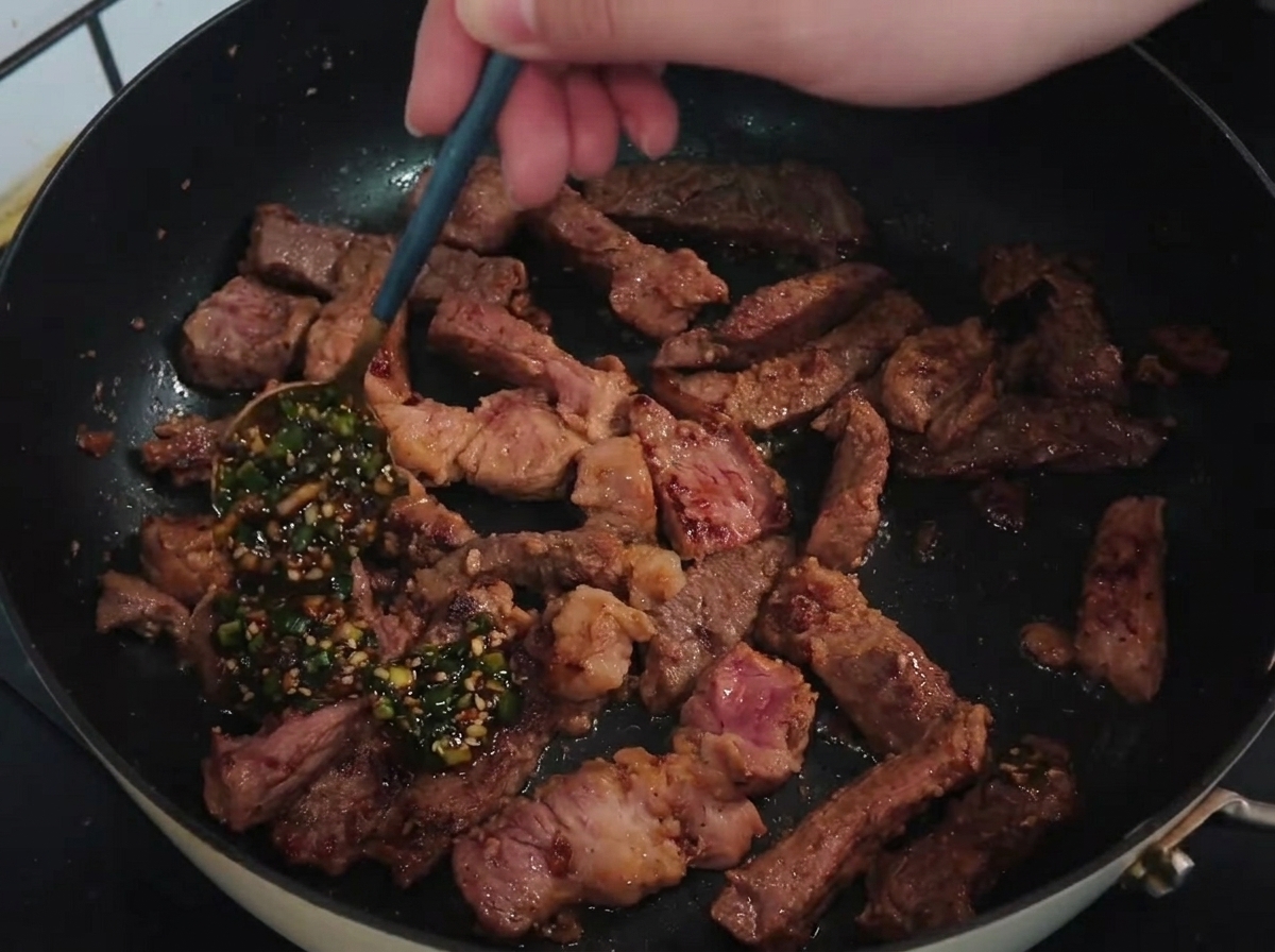 Spoon pouring a vibrant green scallion and garlic sauce over seared, sliced pork chop strips in a hot pan.