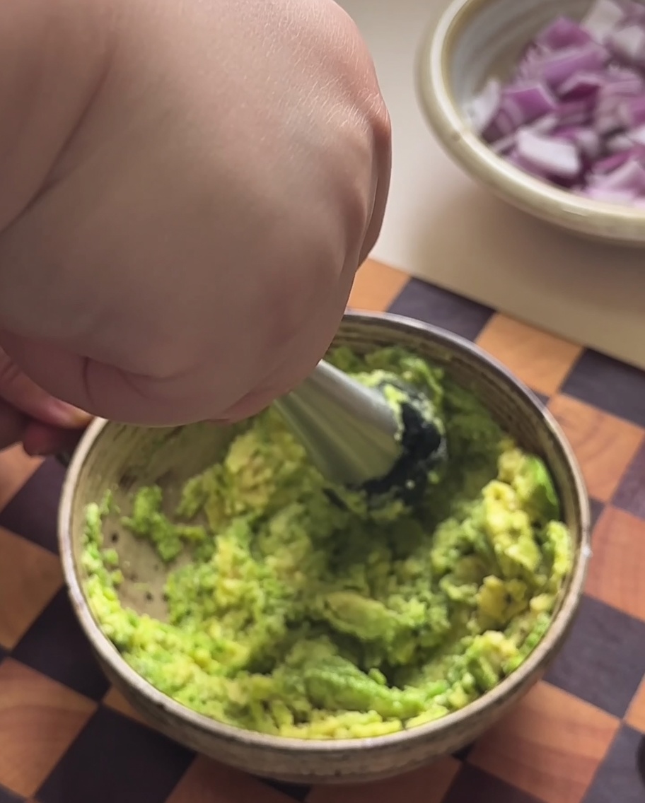 Avocado flesh being mashed into a paste in a bowl.
