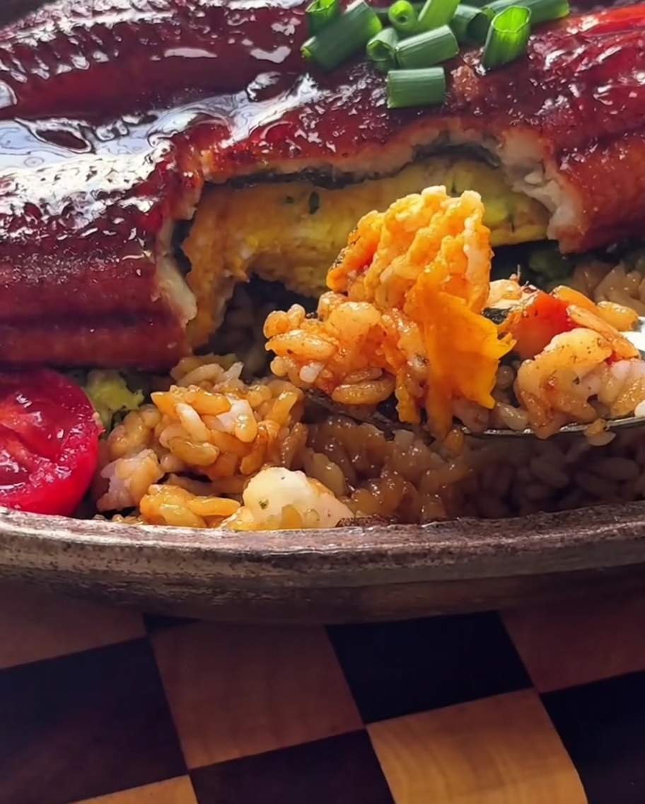 A close-up of a bowl filled with rice, avocado, and other ingredients being seasoned with a sprinkle of seaweed flakes and sesame seeds.