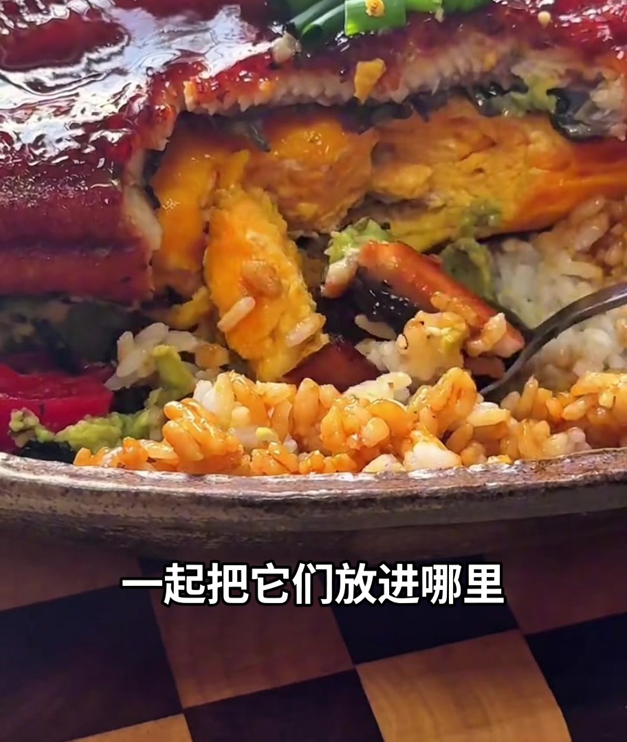 A glazed, roasted eel being transferred with tongs and placed onto the egg-topped rice bowl.