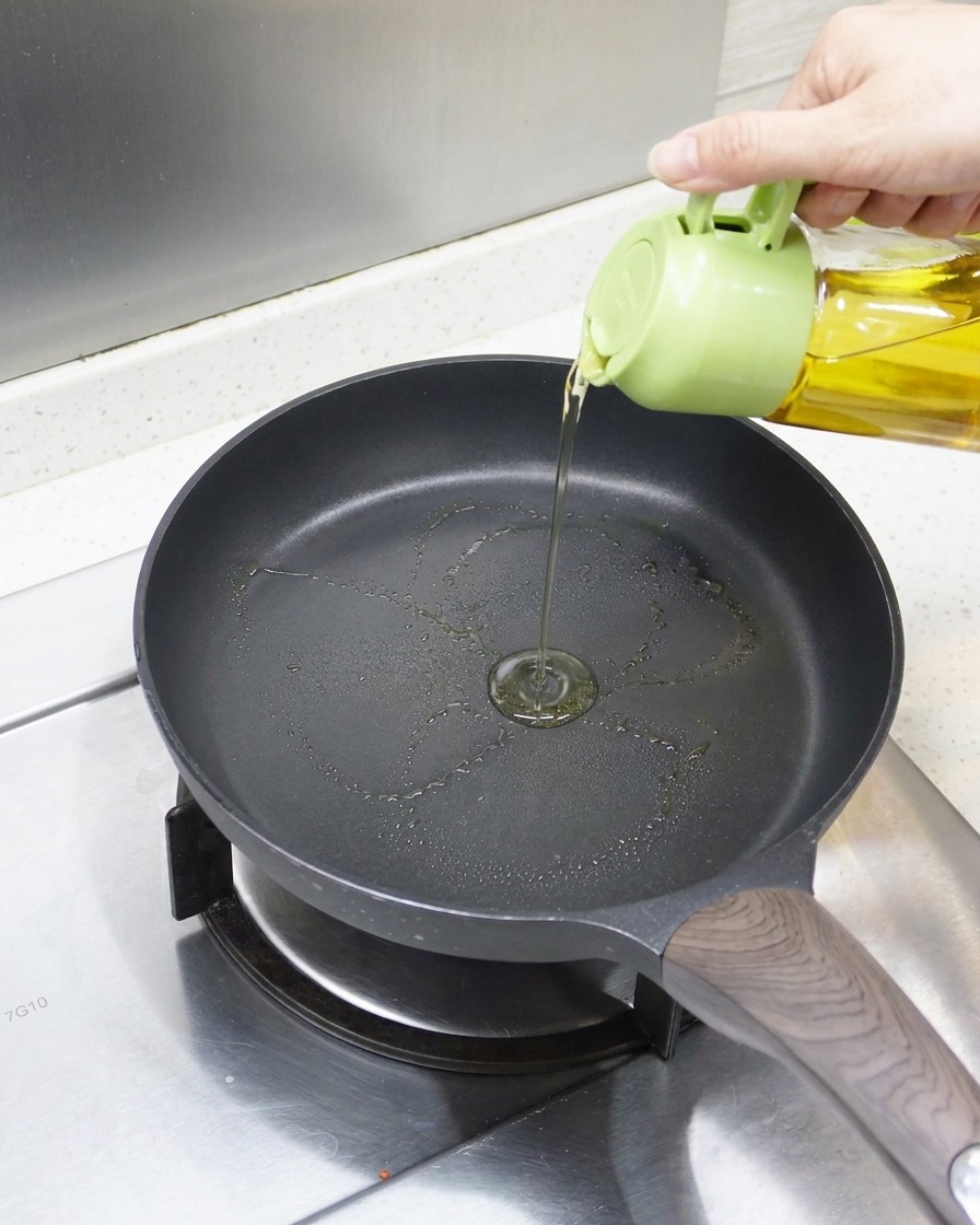 A close-up view of oil being drizzled into a preheated non-stick frying pan, ready for the eel.