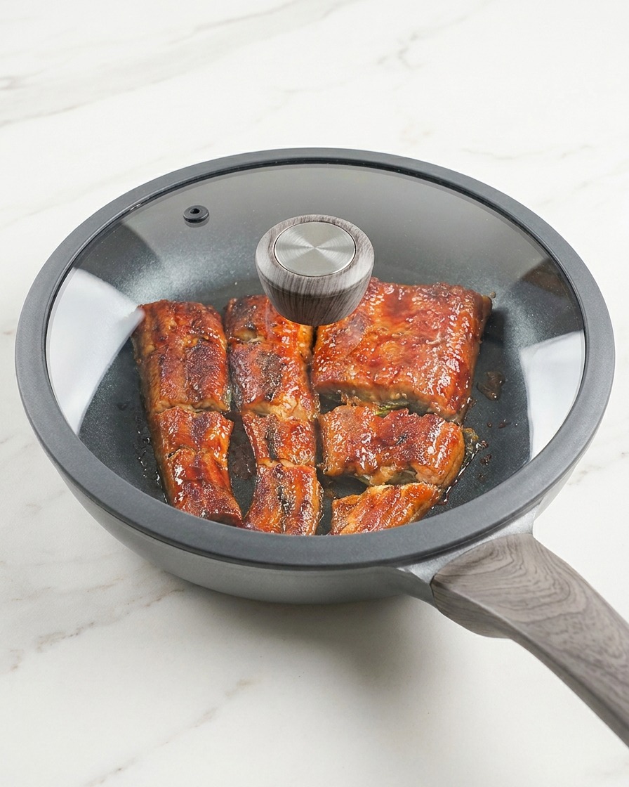 The eel in the pan covered with a glass lid, simmering in the sauce.