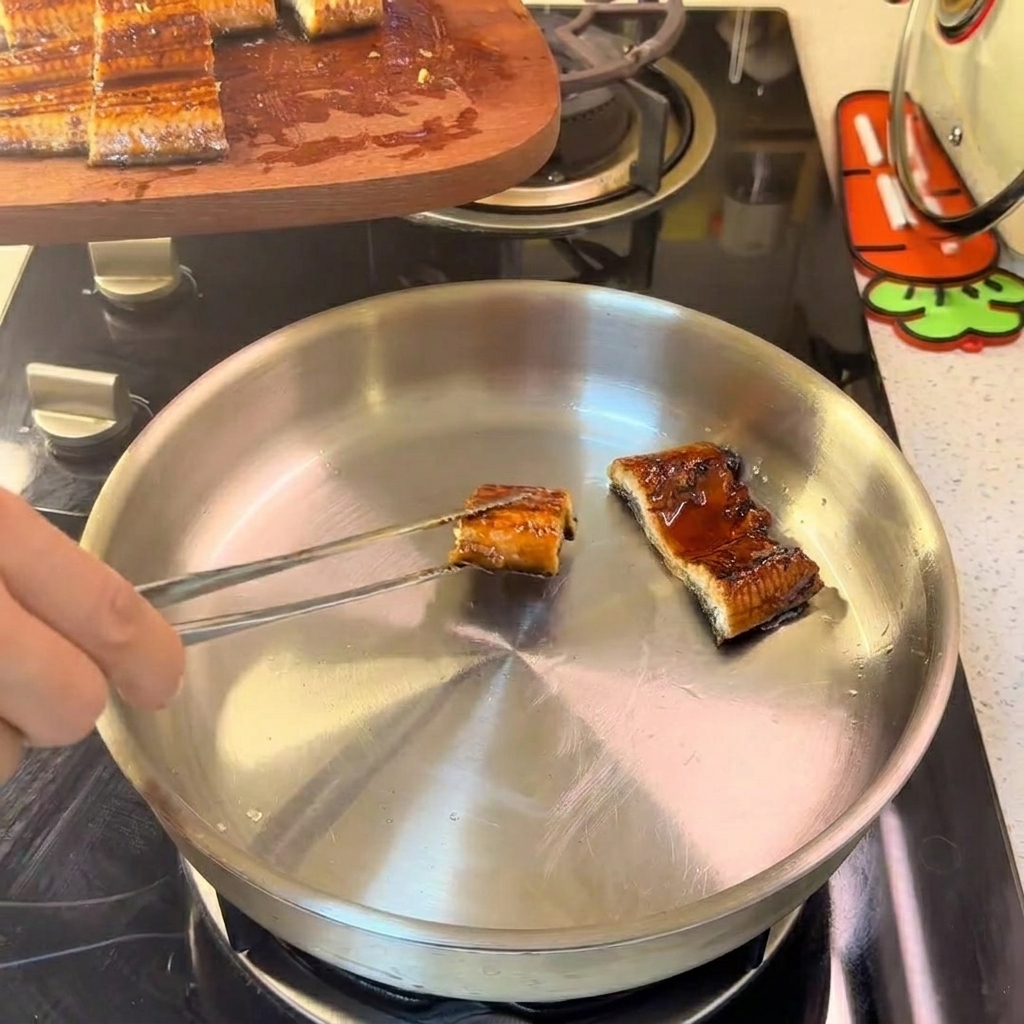Eel pieces arranged in a stainless steel pan, being gently sautéed over a low flame.