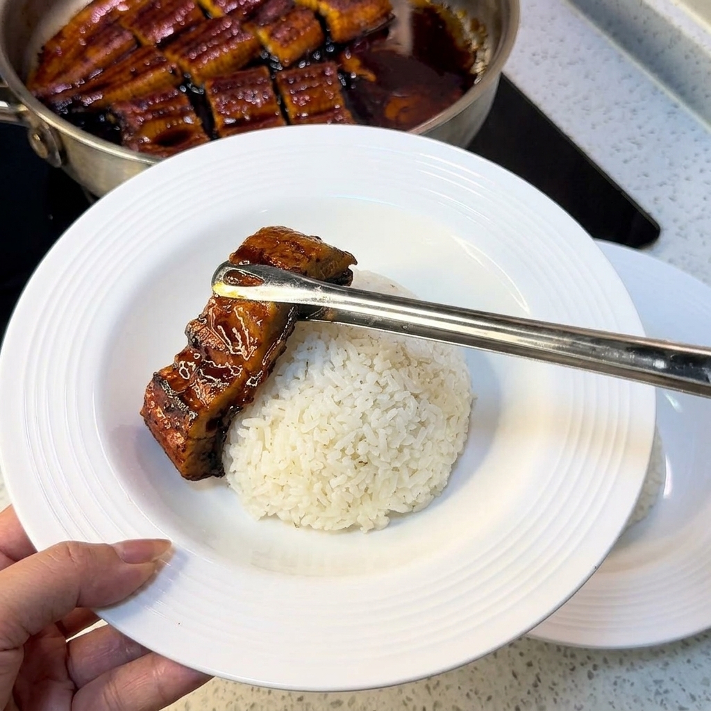 Tongs placing a piece of grilled eel onto a bed of white rice in a white bowl, with egg strips prepared on the side.