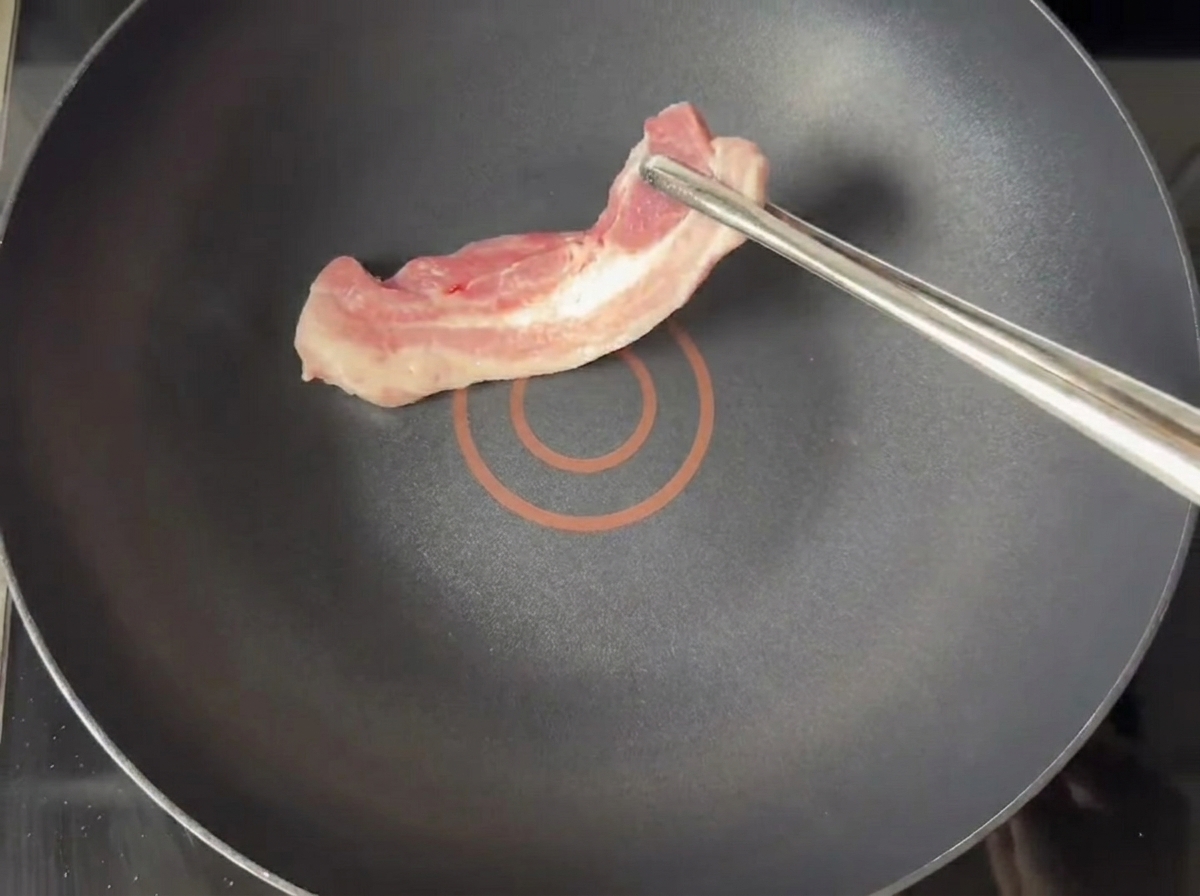Golden brown pork belly slices frying in a dry non-stick pan.