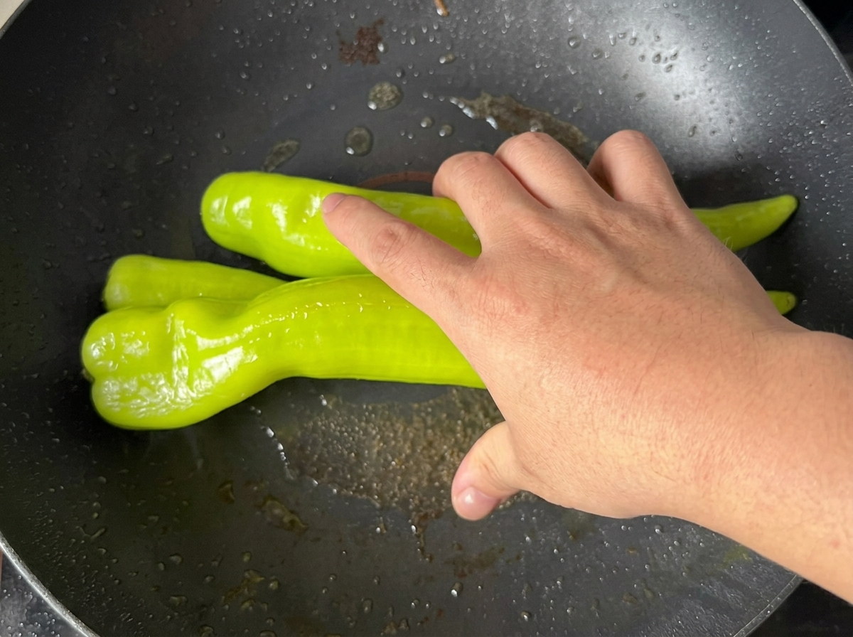 Green peppers frying in a pan until the skin becomes blistered and charred.
