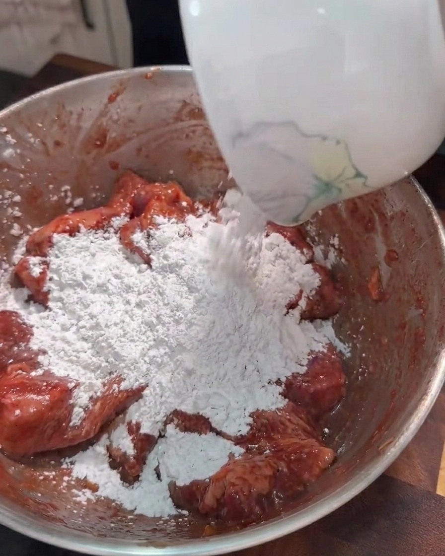 Sweet potato starch being poured into a bowl of marinated pork belly strips.