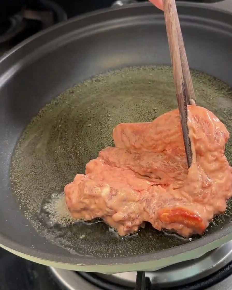 Marinated pork pieces being placed into a pan of hot oil for frying.