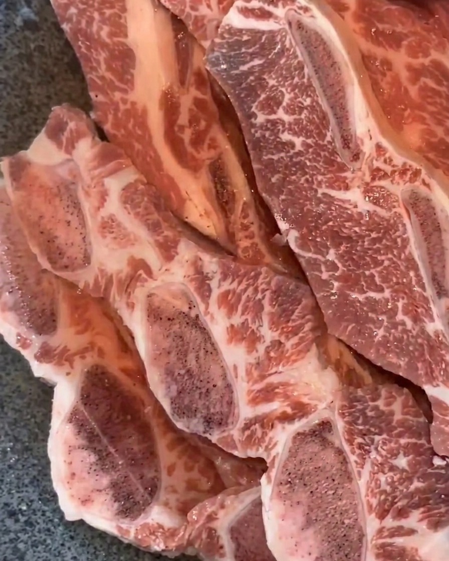 Beef short ribs submerged in water in a metal pan.