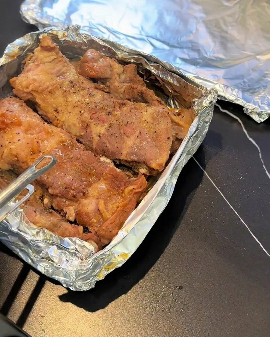 Steamed pork ribs resting on a foil-lined baking sheet, seasoned with black pepper.