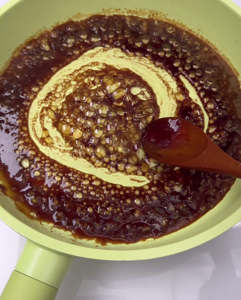 Cooked pork ribs being coated in a rich, dark sauce within a frying pan.