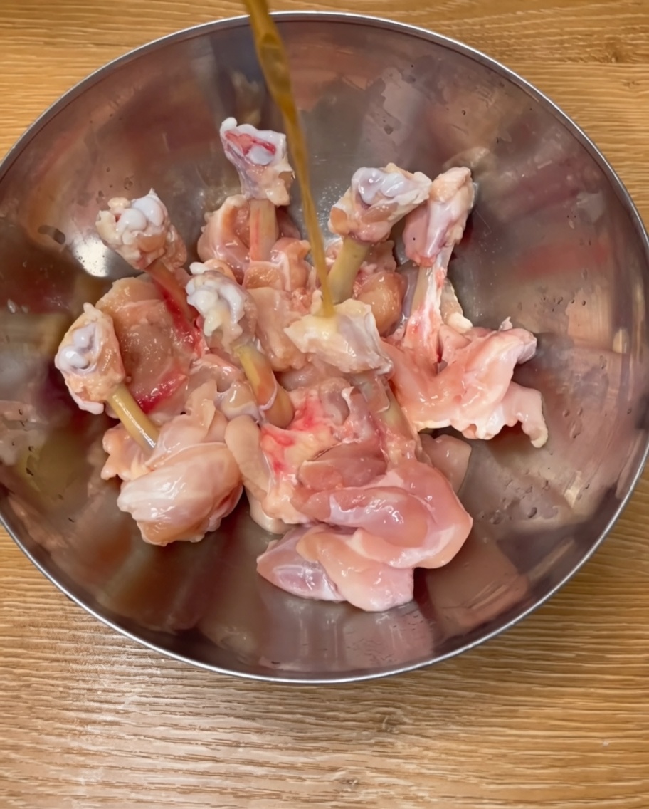 Chicken drumsticks seasoned in a metal bowl with rice wine, spices, and egg liquid.