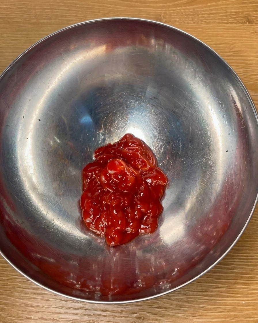 Tomato ketchup and seasonings being mixed in a metal bowl to create a flavorful sauce.